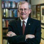 Color photo of Ashby Foote in a suit standing in front of books